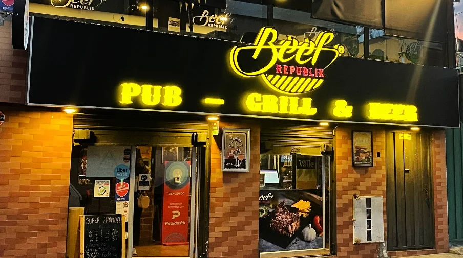 Fachada exterior nocturna del restaurante Beef Republik en Quito, destacando su letrero luminoso de neón amarillo con las palabras Pub - Grill & Beer.