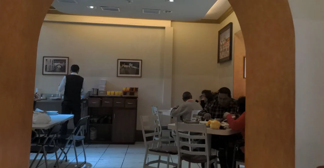 Comedor del Restaurante Benalcázar en Quito visto a través de un arco, con clientes almorzando y cuadros históricos.