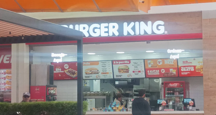 Mostrador de atención y menú digital de Burger King en el patio de comidas de Quicentro Sur, Quito, con promociones de hamburguesas a la parrilla, alitas y combos King Ideal.
