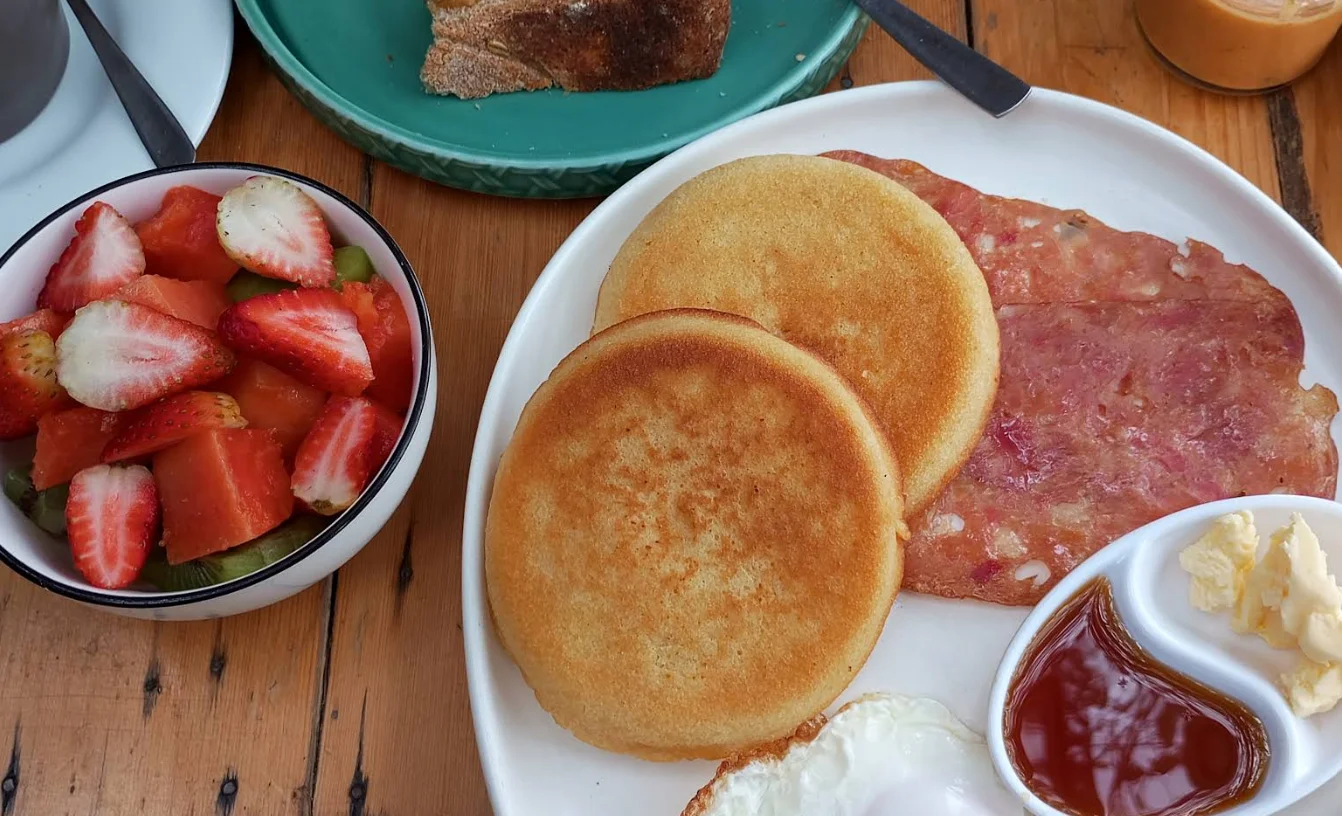 Un plato de desayuno en Casa Warmi con pancakes esponjosos, tocino crocante, ensalada de frutas frescas y miel de abeja.