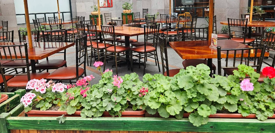 Terraza exterior del restaurante Diosolopay en el Centro Histórico de Quito, con mesas de madera, sillas de hierro y jardines con geranios de colores en el Centro Cultural Metropolitano.