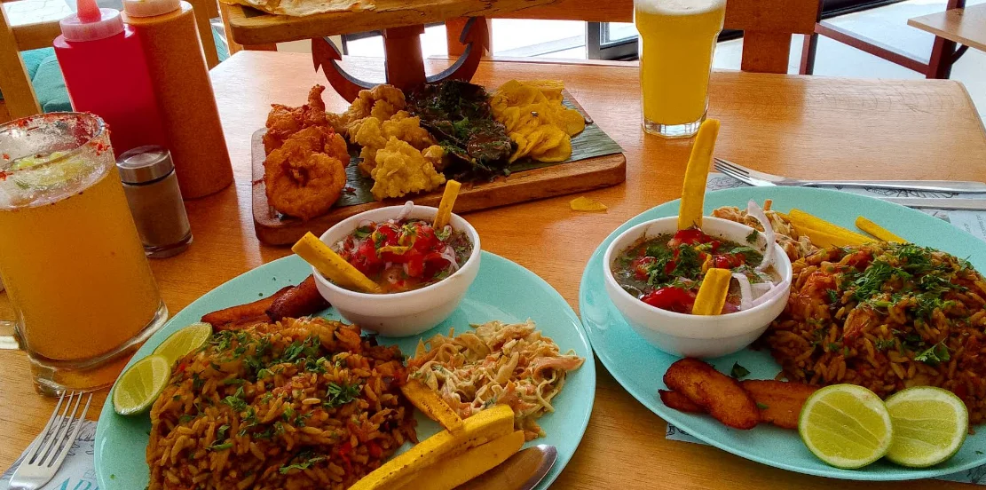 Abundante festín de mariscos en el restaurante El Arrastre en el Sur de Quito, mostrando platos de arroz marinero, ceviche fresco, chifles, mariscos fritos y bebidas refrescantes tipo michelada.