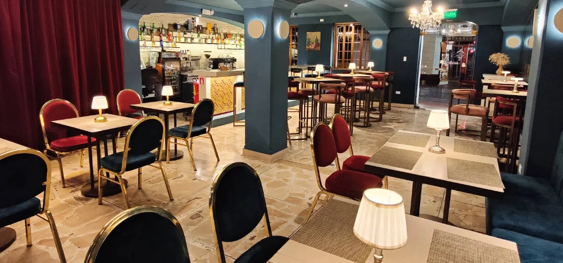 Salón interior del restaurante El Criollo en el Centro Histórico de Quito: ambiente elegante con sillas de terciopelo rojo y azul, lámparas de mesa, araña de cristal y barra de licores al fondo.