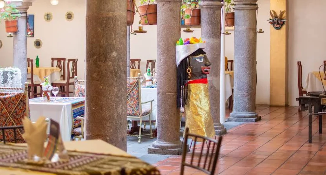 Salón colonial de La Capilla Restaurant en el Centro Histórico de Quito: columnas de piedra, figura de gigante de Quito, manteles bordados y decoración artesanal ecuatoriana.