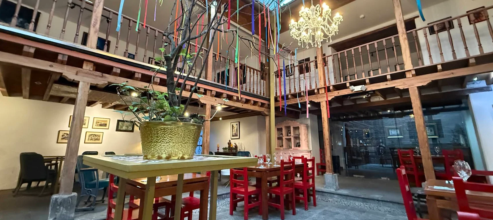 Interior colonial del Restaurante La Purísima con patio central cubierto, balcones de madera tallada y distintivas mesas rojas.