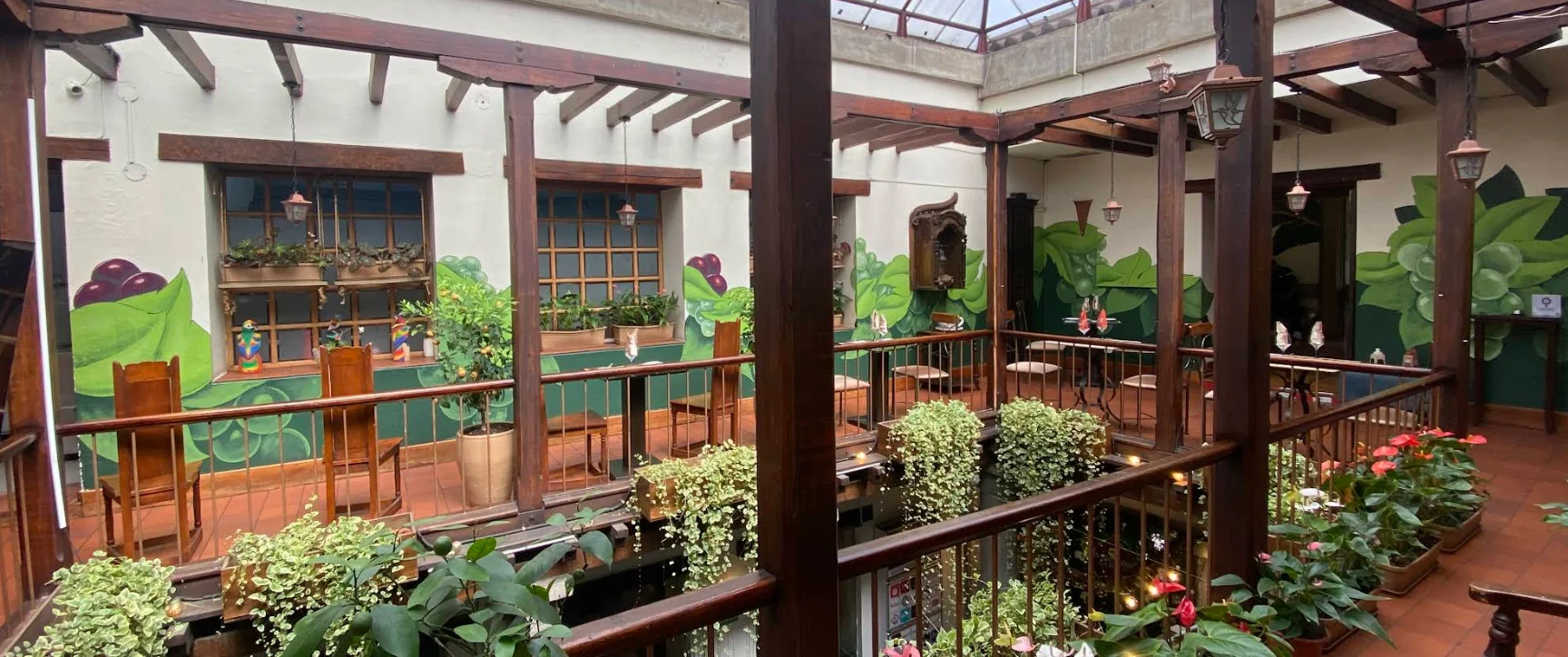 Balcón interior del restaurante La Vid en Quito con vigas de madera, murales de hojas verdes y abundantes plantas decorativas.