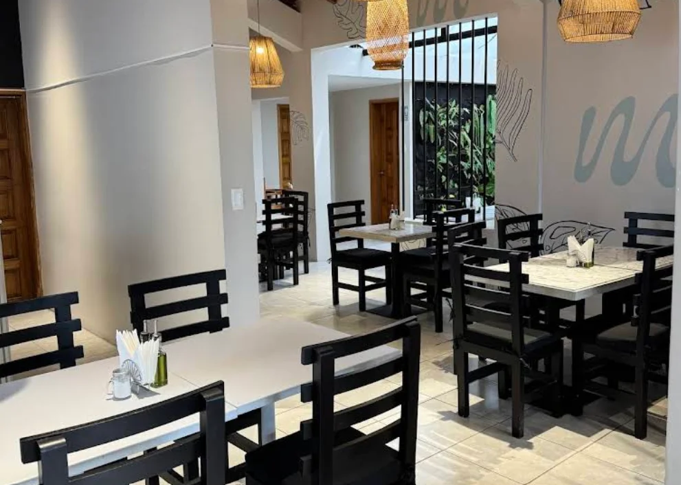 Vista interior del amplio comedor del restaurante Macchiata, destacado por sus grandes arcos de ladrillo visto, iluminación cálida de guirnaldas de luces y filas ordenadas de mesas y sillas de madera.