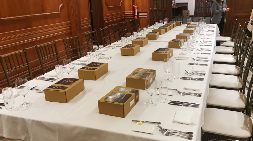 Larga mesa de banquete en el restaurante Marcus, preparada con mantel blanco, cajas individuales en cada puesto y paredes de madera.