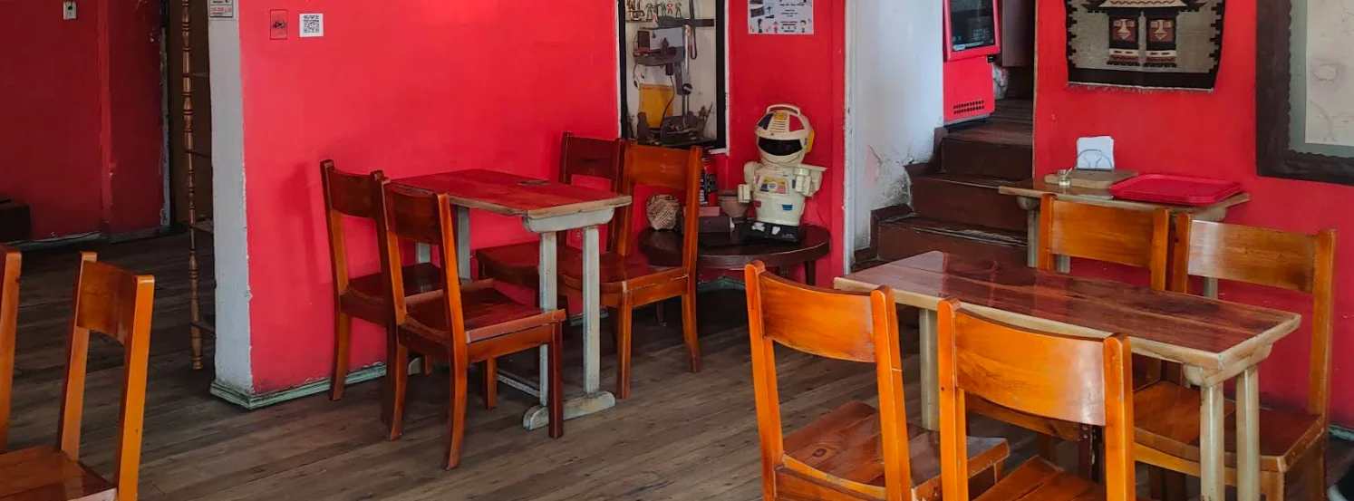 Interior rústico del restaurante Mote Colonial con mesas de madera, paredes rojas y decoración vintage.