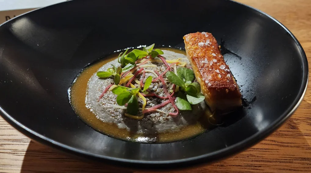 Plato de alta cocina con crema, panceta crocante y microgreens en NUEMA, restaurante en Quito.