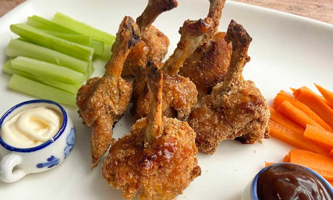 Plato de alitas de pollo estilo lollipop glaseadas con bastones de apio, zanahoria y salsas en Restaurante Querubín Quito.