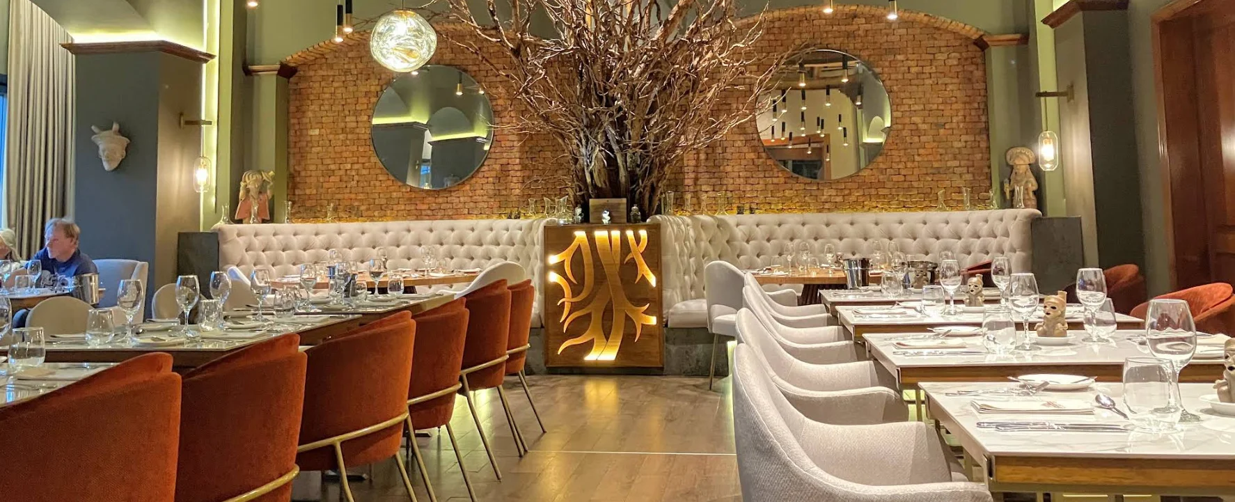 Salón principal del restaurante Raíces en Quito con pared de ladrillo, espejos circulares y una escultura central de madera iluminada con forma de raíces.