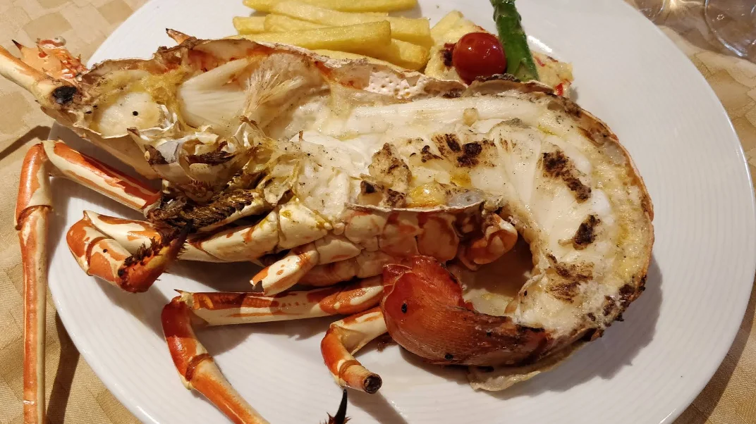 Langosta a la parrilla partida con papas fritas y espárragos, plato de alta cocina francesa en Rincón de Francia, Quito.