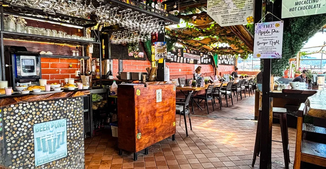 Interior del Rooftop Bar and Restaurant del Secret Garden en Quito, con barra de ladrillo visto, copas colgantes, menú en pizarra y terraza cubierta de vegetación con vista al Centro Histórico.