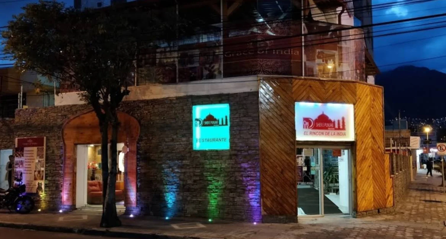Fachada iluminada del restaurante indio Sher E Punjab en Quito, con paredes de piedra y madera por la noche.