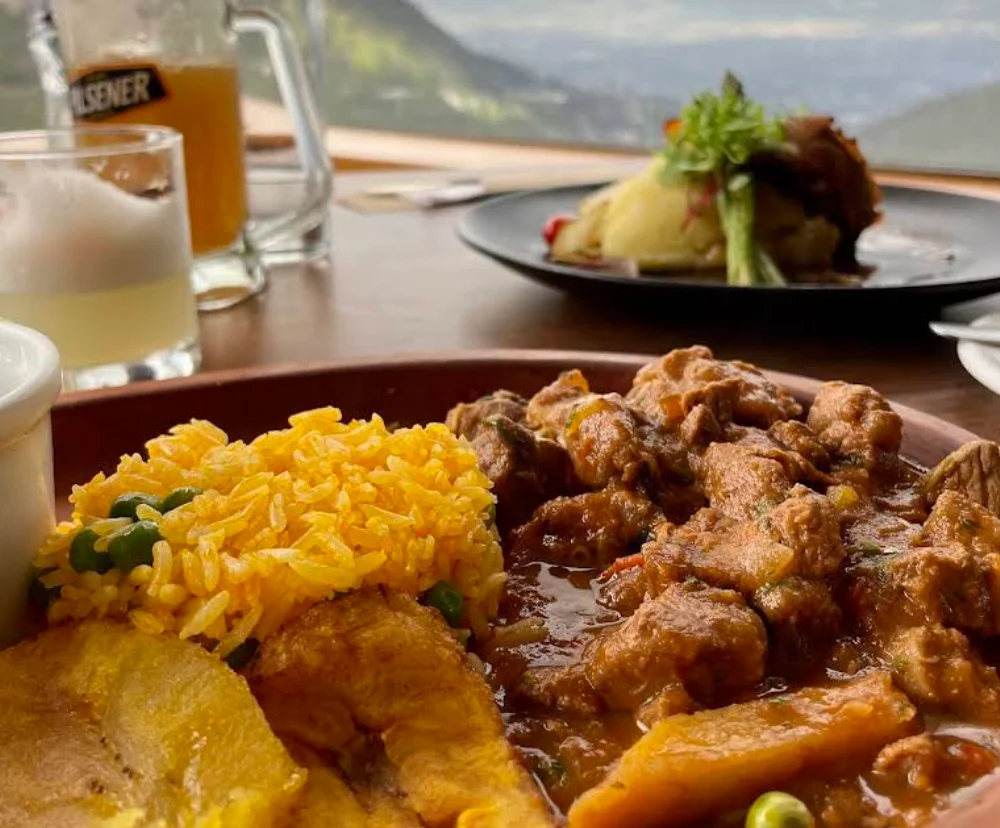 Plato de seco de carne colorada con arroz y patacones en Restaurante Techo del Mundo, Quito con vista al valle.