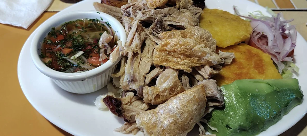 Hornado de cerdo con cuero crocante, llapingachos, aguacate, ensalada de cebolla y ají de tomate, plato típico ecuatoriano servido en Vicente's en la Mitad del Mundo, Quito.