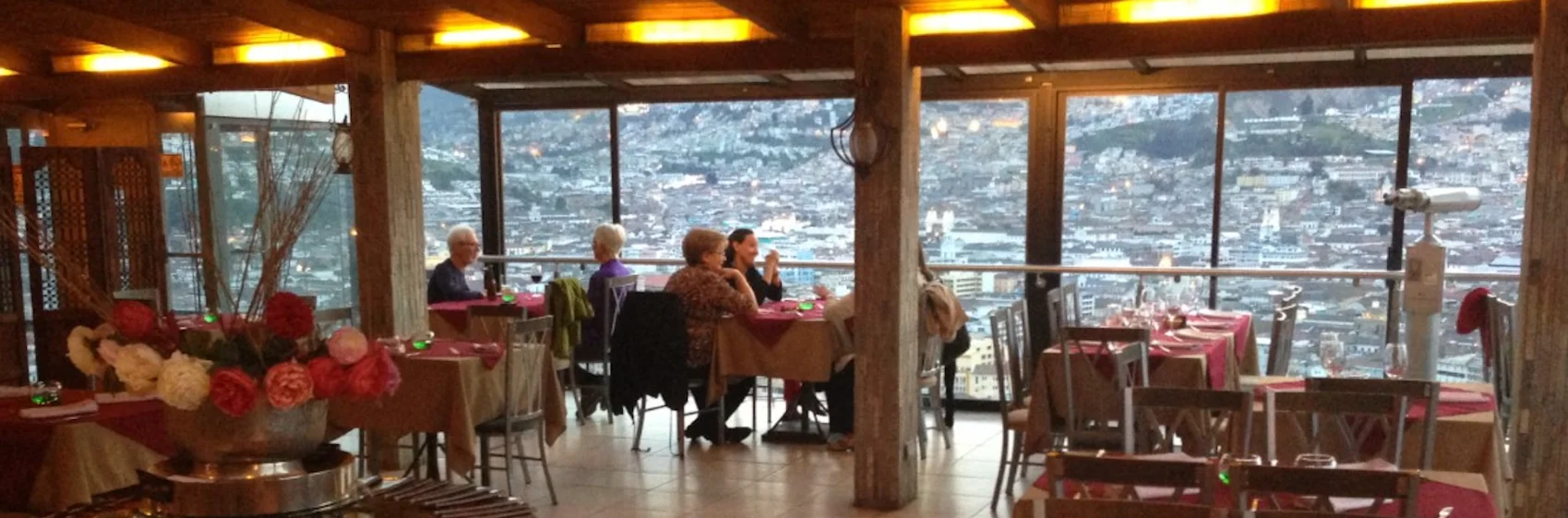 Comedor del restaurante Vista Hermosa Itchimbia con amplios ventanales que ofrecen una vista panorámica del Centro Histórico de Quito al atardecer.